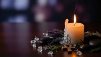 Burning candle with pentagram pendant, crystals and evergreen branches creating mystical altar setup for spiritual practices and meditation rituals.