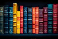 Row of vintage leather-bound books with gold embossed spines in various colors including blue, yellow, and red against dark background, showing classic library collection.