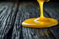 Golden honey dripping from wooden dipper onto rustic dark wood surface creating smooth flowing stream against textured background for culinary designs.