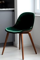 Modern emerald green velvet dining chair with wooden legs against white wall background, minimalist contemporary furniture design for home interior.