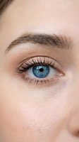 Close-up of woman's blue eye with natural makeup and well-groomed eyebrow showing detailed iris patterns and long eyelashes on smooth skin.