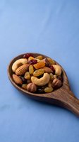 Mixed nuts and dried fruits in wooden spoon on blue background. Healthy snack mix with cashews, almonds, hazelnuts, raisins and cranberries for nutrition concepts.