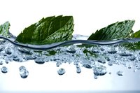 Fresh mint leaves floating on crystal clear water surface with rising bubbles, dynamic splash effect creating refreshing and pure beverage concept.