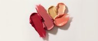 Colorful lipstick smears and swatches on white background showing various shades of pink, coral and nude tones for cosmetic makeup applications.