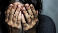 Asian woman covering face with hands in dark moody lighting, expressing deep emotional distress, grief, depression, and vulnerability. Dramatic shadows emphasize isolation.