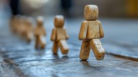 Wooden figurines walking in line on textured surface, shallow depth of field creates artistic blur effect, representing leadership and following concept.