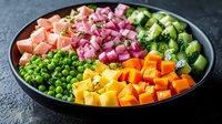 Fresh colorful chopped vegetables and salmon arranged in rows on black plate, including peas, cucumber, butternut squash, red onion and herbs on dark background.