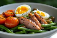 Grilled salmon fillet with soft-boiled eggs, cherry tomatoes and green beans on white plate, close up view of healthy protein-rich dinner meal.