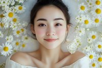Young Asian woman with natural makeup smiling while lying among fresh white daisies, representing beauty, wellness and natural skincare concepts.