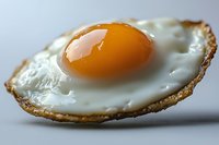 Close-up macro shot of sunny side up fried egg with crispy brown edges and bright orange yolk on light background, showing texture and detail of breakfast food.