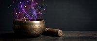 Ancient brass singing bowl with wooden mallet releasing mystical purple energy and sparkling particles on dark background for meditation and healing practices.