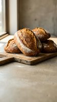 Freshly baked artisan sourdough bread loaves on wooden cutting board in rustic kitchen setting with natural window light for bakery and food photography.