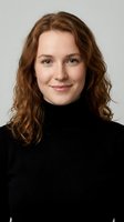 Young Caucasian woman with curly brown hair wearing black turtleneck sweater smiling at camera against neutral background for professional headshot.