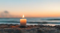 Glowing candle on sandy beach at sunset with blurred ocean waves and warm sky background creates peaceful meditation atmosphere.