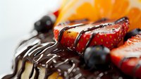 Fresh strawberries and blueberries on chocolate glazed dessert with orange slices, extreme macro close up showing texture and dripping chocolate sauce.