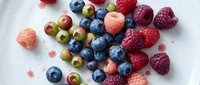 Fresh mixed berries including raspberries, blueberries, and gooseberries arranged on white marble surface for food styling and culinary projects.