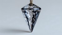 Crystal pendant with faceted diamond shape hanging from brown cord against neutral gray background, showcasing light reflections and transparency.