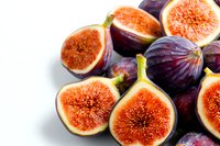 Fresh ripe purple figs cut in half showing juicy pink flesh and seeds on white background, macro food photography for healthy eating and recipe blogs.