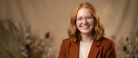 Professional young Caucasian businesswoman with red curly hair and glasses smiling confidently in modern office environment for corporate presentations.