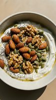 Creamy yogurt bowl topped with almonds, walnuts, pumpkin seeds, and poppy seeds drizzled with olive oil for healthy breakfast or snack.