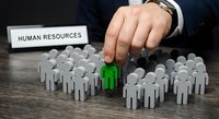 Professional businessman selecting green figure from crowd of white paper cutouts representing talent acquisition and recruitment process for human resources department.