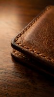 Brown leather wallet with hand-stitched edges on wooden surface showcasing traditional craftsmanship and quality materials for luxury accessories.