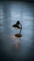 Vintage desk lamp with glowing bulb on concrete floor in moody industrial setting, suitable for interior design, product photography, and creative workspace concepts.
