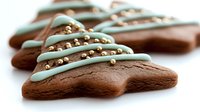 Chocolate tree-shaped cookies decorated with mint green icing drizzle and gold sugar pearls on white background, festive holiday baking treat for Christmas season.