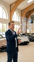 Middle-aged Caucasian businessman in suit interacting with futuristic holographic interface in luxury car showroom with modern architecture and vehicles.
