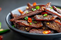 Spicy glazed beef strips with chili peppers and green onions in black bowl, Asian cuisine dish ready for restaurant menu or food blog content.