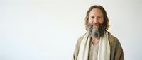 Smiling middle-aged Caucasian man with long gray beard and hair wearing casual beige cardigan against white background for lifestyle content.