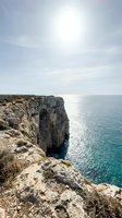 Dramatic limestone cliff face overlooking turquoise Mediterranean waters under bright sunlight, showcasing rugged coastal landscape and natural rock formations for travel and nature content.