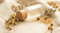 Natural cosmetic serum bottle with wooden cap surrounded by dried chamomile flowers on linen fabric for organic skincare and beauty treatments.