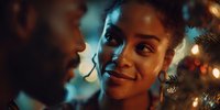 Young African American woman smiling at partner during intimate holiday celebration with Christmas lights creating warm, romantic atmosphere.