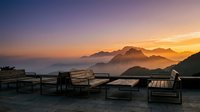 Wooden lounge chairs on a waterfront deck overlooking misty mountains at sunrise, perfect for travel and hospitality design projects.