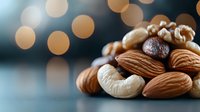 Mixed raw nuts and coffee bean with soft bokeh lights in background, selective focus on almonds and cashews creates appetizing composition for food photography.