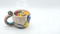Whimsical ceramic mug with octopus tentacle handle and colorful interior design, isolated on white background for product design and merchandise applications.
