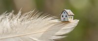 Miniature house model sitting on soft white feather with blurred natural background, concept for home protection, real estate dreams and property investment.