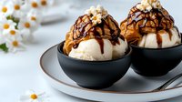 Vanilla ice cream scoops in black bowls topped with caramel sauce, chocolate drizzle and popcorn garnish, served on ceramic plate with floral decoration.