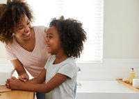 Happy African American mother and daughter embracing in bright modern bathroom, showing love and family bonding moments at home.