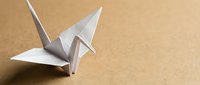 White origami paper crane on a warm brown kraft paper background with copy space, symbolizing peace, creativity, and Japanese tradition.