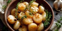 Roasted pearl onions garnished with fresh thyme sprigs in rustic ceramic bowl. Golden caramelized vegetables with herbs create appetizing side dish.