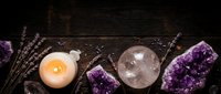 Amethyst crystals, clear quartz sphere, and glowing candle with dried lavender on dark rustic wood, flat lay spiritual wellness arrangement.