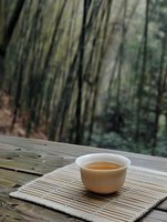 Traditional ceramic tea cup with amber tea on bamboo mat outdoors with natural forest background for mindful drinking and relaxation moments.