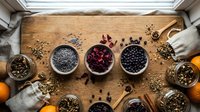 Hands in white gloves arranging various spices, herbs and dried ingredients in bowls on rustic wooden cutting board for culinary preparation.