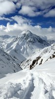 Majestic snow-covered mountain peak rising against dramatic blue sky with white clouds, fresh powder snow in foreground creating natural winter landscape.