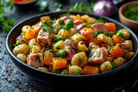 Roasted potato, pumpkin and salmon chunks with fresh dill and red onion in cast iron pan, rustic food styling on dark background. Seasonal autumn dish.