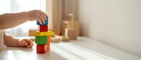Child hands building colorful wooden block tower on white table in bright playroom. Educational toy development activity for kids learning.