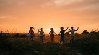 Silhouettes of diverse children holding hands in circle at golden sunset in open field, celebrating friendship and unity outdoors.