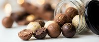 Assorted chocolate truffles spilling from glass jar with warm bokeh lights creating luxurious confectionery display for gourmet dessert marketing.